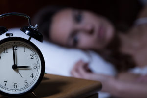 A woman lies in bed, staring at her alarm clock.