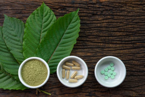 Three bowls contain kratom, a safe alternative to opioid painkillers. Kratom takes four forms: small circular pills, large tube-shaped pills, powder, and leaves.