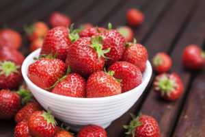A white bowl holds a bunch of red strawberries.