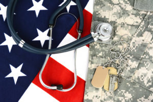 A stethoscope lies on top of an American flag and a U.S. Army field jacket.