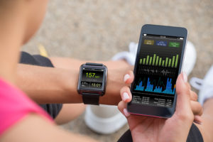 A person looks at their cellphone and watch. Both devices appear to be tracking their fitness data.