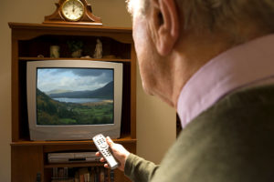 An elderly adult uses a remote to turn on his TV.