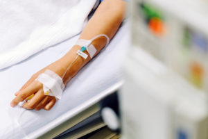 A woman's arm is shown attached to an IV as she lies in a hospital bed.