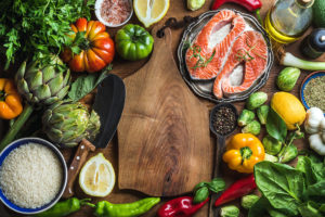Rice, vegetables, salmon, olive oil, citrus fruit and spices are shown. All of the ingredients are being prepared for a Mediterranean diet meal.