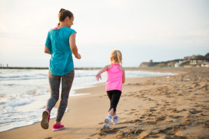 A mother runs along the beach with her young daughter.