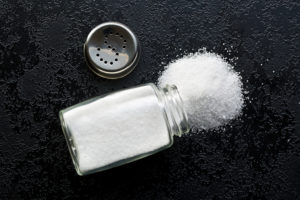 A salt shaker spills out salt. The lid of the salt shaker is off.