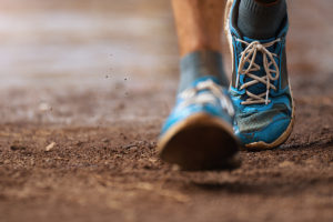 A person wearing blue tennis shoes is running outside.