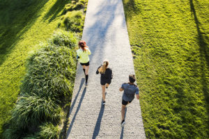 Three people run outside together on a pathway.