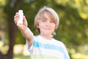 A young boy holds up his quick-relief asthma inhaler and smiles.