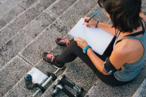 A woman writes into a journal as she sits on a few steps outside.