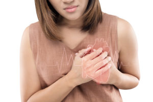 A woman holds her hands over her heart and appears uncomfortable. An illustration of a heart rate is shown in front of her chest.
