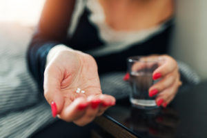 A woman holds sleeping pills in her hand and gets ready to take them with water.