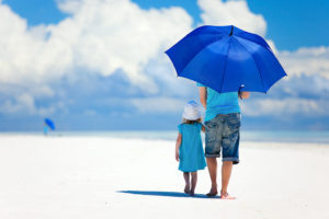 An adult and child walk along the beach with an umbrella.