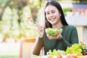 A young teenager eats a salad and smiles as she sits outside.