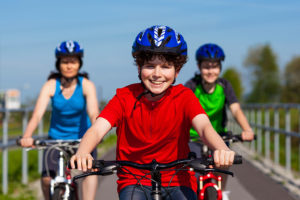Three kids ride their bikes outside together and wear a helmet.
