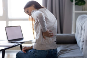 A woman holds her back and appears in pain.