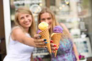 Two woman hold up their ice cream cones and pose for a photo.