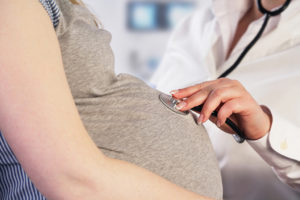 A doctor places a stethoscope on a pregnant woman's belly.
