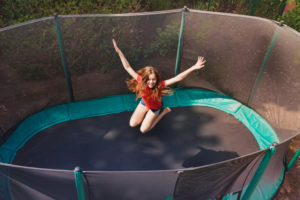 A young girl jumps on a trampoline. The trampoline safety net surrounds her.