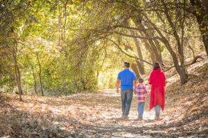 A family walks in a public park together, holding hands.