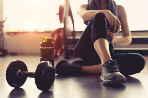 A woman sits on the floor next to dumbbell weights at the gym.