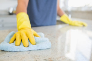 A person wearing yellow gloves washes their kitchen countertop with a towel.