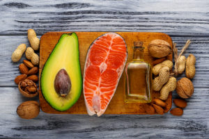 Different types of nuts, an avocado, a piece of salmon and a bottle of olive oil is shown.