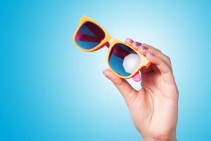 A person holds a pair of orange sunglasses.