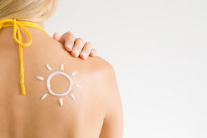 A woman applies sunscreen on her shoulder.
