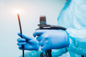 A person wearing medical gloves holds a colonoscopy device.