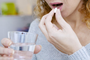 A woman takes a prescribed medication with a glass of water.