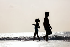 Two children walk along the beach.
