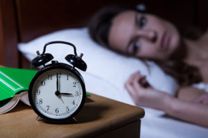 A woman lies in bed and stares at her alarm clock.