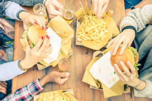 A group of people eat hamburgers and french fries at a picnic table.