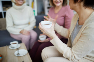 A group of women sit at a coffee shop together and chat. They all have a cup of coffee.