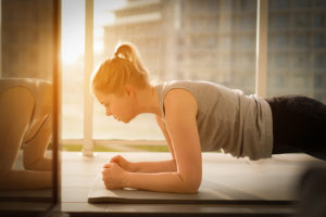 A young woman does a plank on an exercise mat inside her apartment.