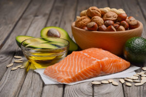 Salmon, avocado, a variety of nuts and olive oil are placed next to each other on a table.