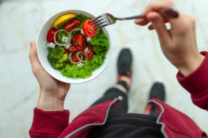 A person eats a salad with a fork. The salad contains tomatoes, onions, broccoli and a light dressing.