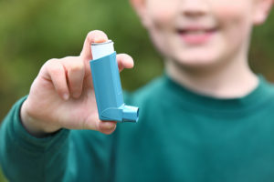 A young boy holds up an inhaler and smiles.