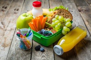 A lunch box contains fruits, vegetables and a vegetarian sandwich.
