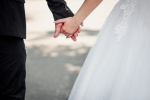 A woman in a wedding dress holds hands with her husband.