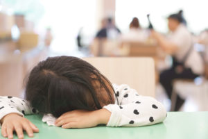 A young girl lies her head on her desk and falls asleep. She appears sleep deprived.