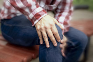 A person sits down and grabs his knee in pain.