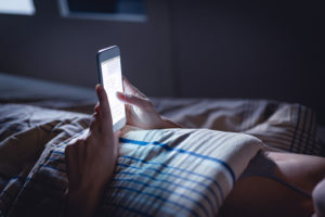 A person lies in bed and stares at their smartphone instead of sleeping.