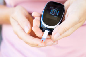 A woman holds a blood glucose monitor in her hands.