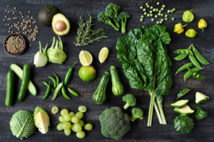 Leafy green plants and cruciferous veggies are shown; including but not limited to an avocado, lime, green grapes, broccoli, cucumber and snap peas.