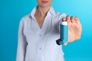 A person holds up a blue inhaler and shows it off.