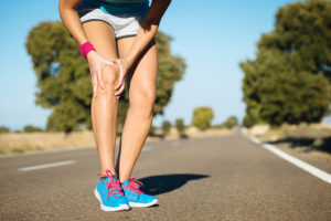 A runner leans down and grabs their knee. They appear in pain.