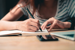 A woman writes a list into her journal with a black pen.
