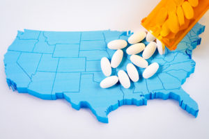 Pills from a prescription bottle are poured onto a map of the United States, symbolizing the opioid epidemic.